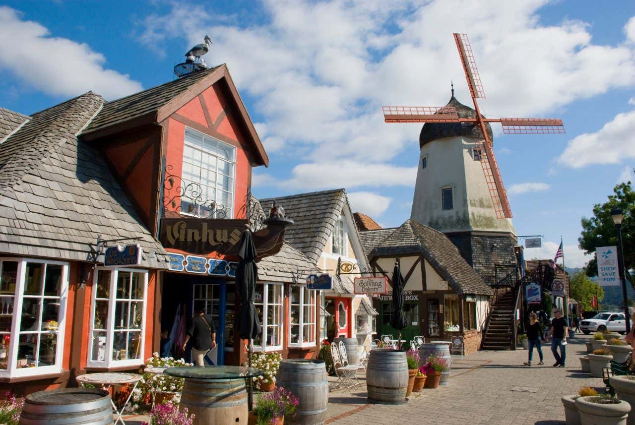 A number of traditional buildings in Solvang and a windmill and a cloudy sky in the background.