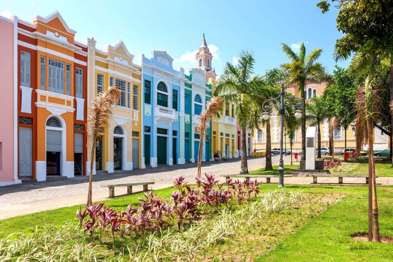 Construções coloridas em estilo colonial em uma praça com árvores e flores