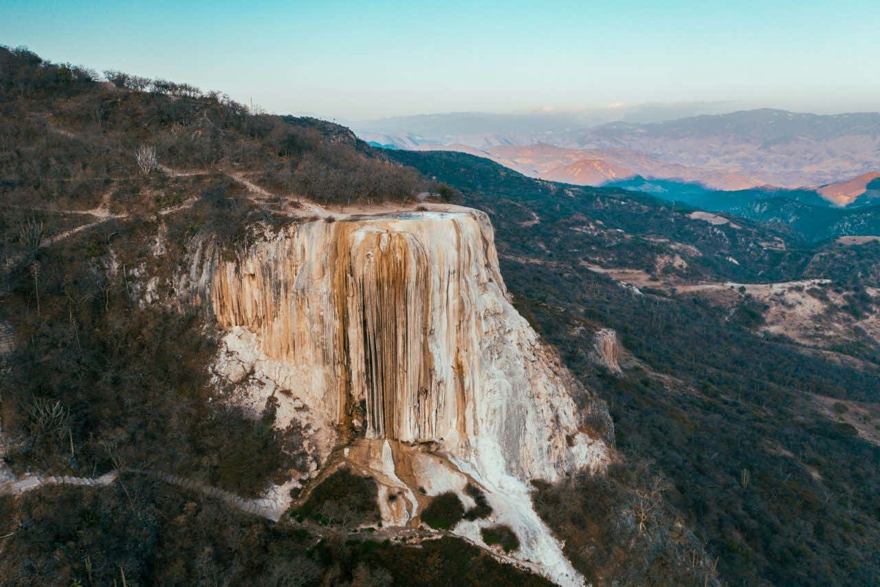 Hierve el Agua waterfall as seen from afar with a light blue sky in the background.