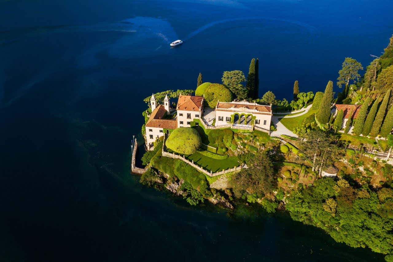 Vista aerea di Villa Balbianello, posizionata su un piccolo promontorio affacciato sulle placide acque del Lago di Como. È composta da un edificio principale che da proprio sull'acqua, e una dependance in cima al colle, circondata da un giardino ben curato con aiuole e alberi