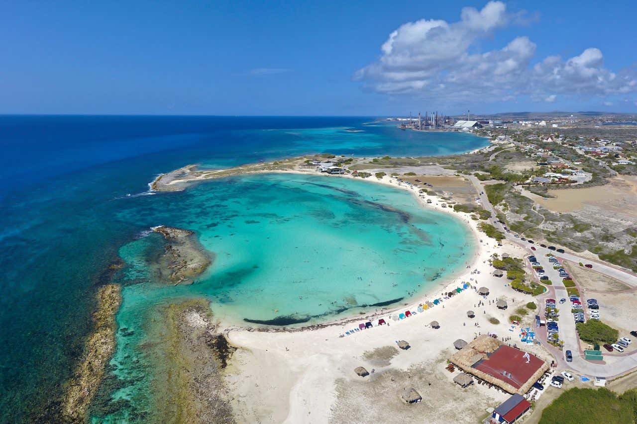 Vista aérea de da praia Baby Beach em formato semi-lua com areia branca e águas turquesas