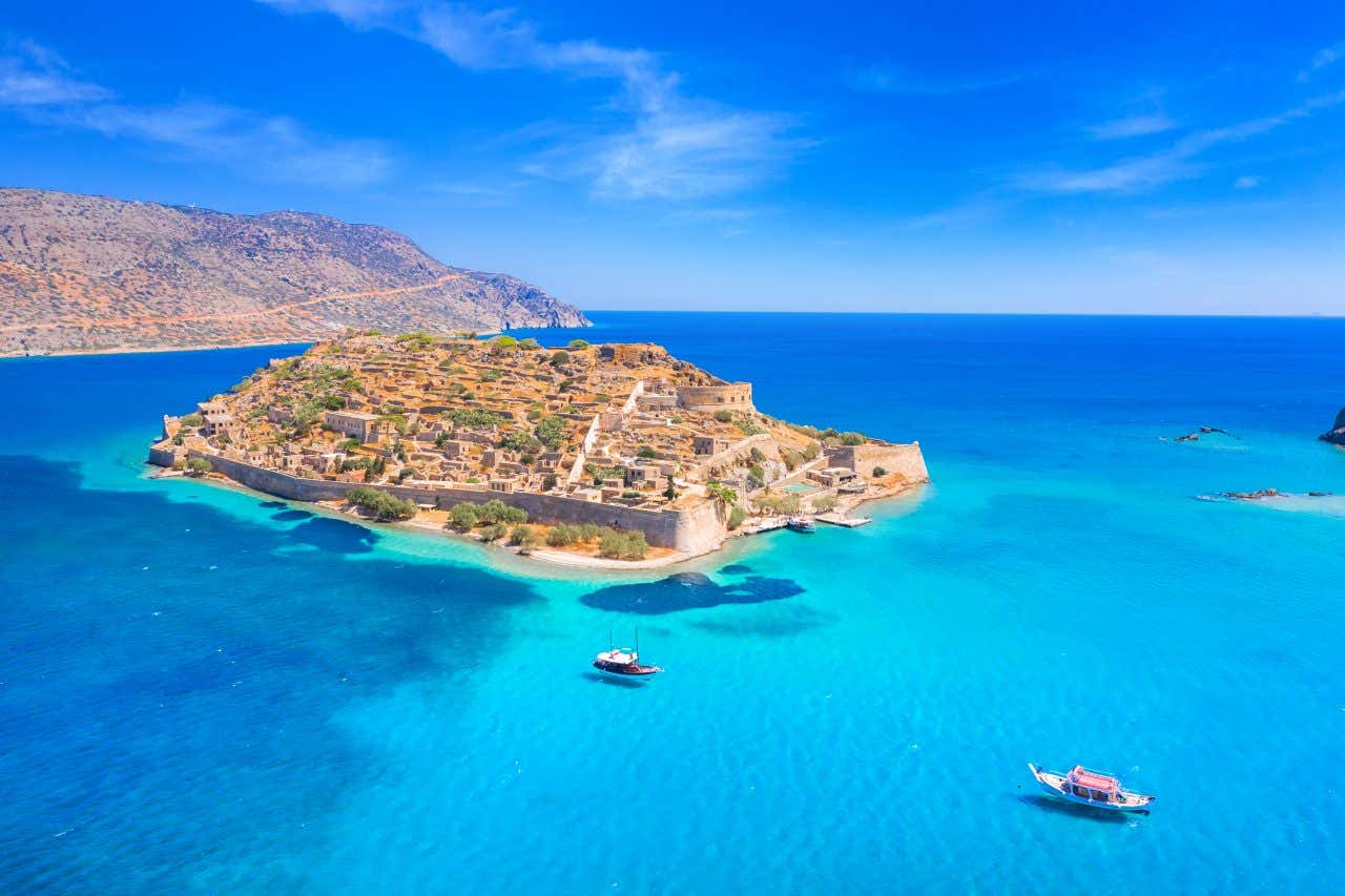 Veduta aerea dell'isola di Spinalonga a Creta, Grecia, con le sue rovine storiche circondate da mura fortificate, acque turchesi e barche ormeggiate nelle vicinanze