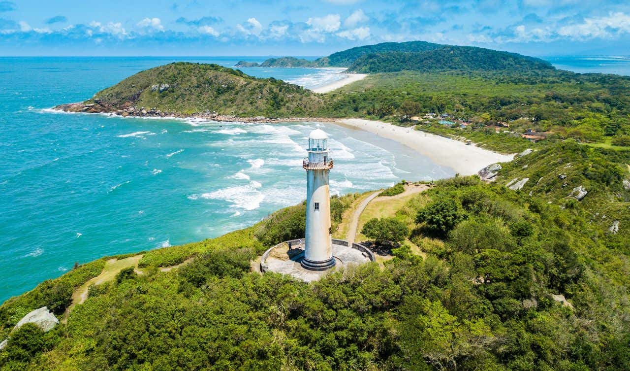 Vista aérea com águas turquesas e rodeado de vegetação e destaque para o Farol das Conchas