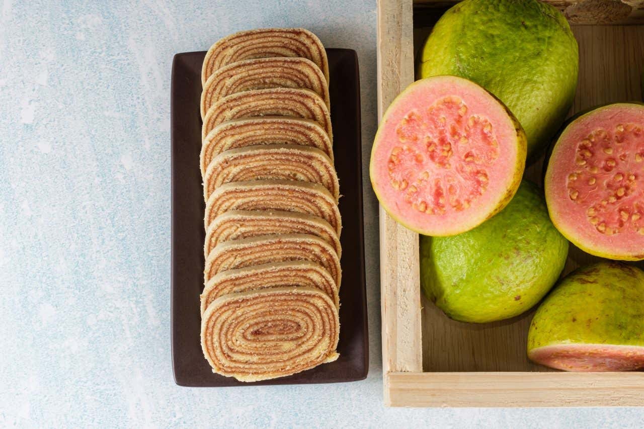 Um prato com fatias de bolo de rolo ao lado de uma caixa com goiabas