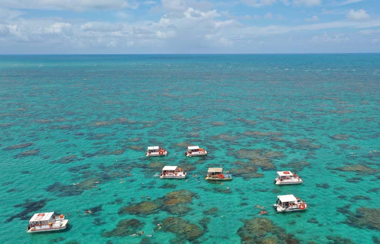 Maravilhosa vista panorâmica dos recifes de coral de Maracajaú com vários barcos de turismo flutuando em águas azul turquesa perto da cidade de Natal, Rio Grande do Norte, Brasil