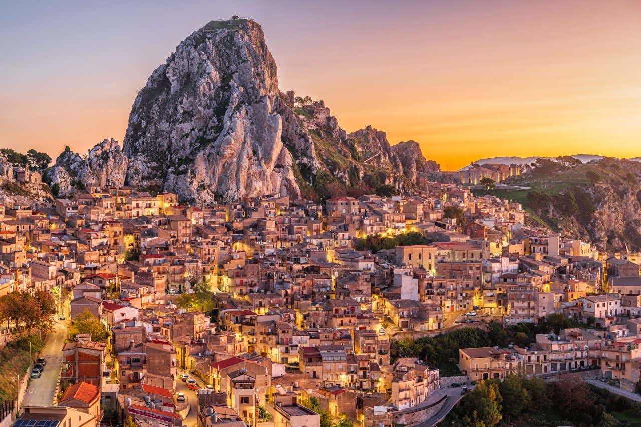 A Sicilian city seen from above with a pink and orange sky in the background.