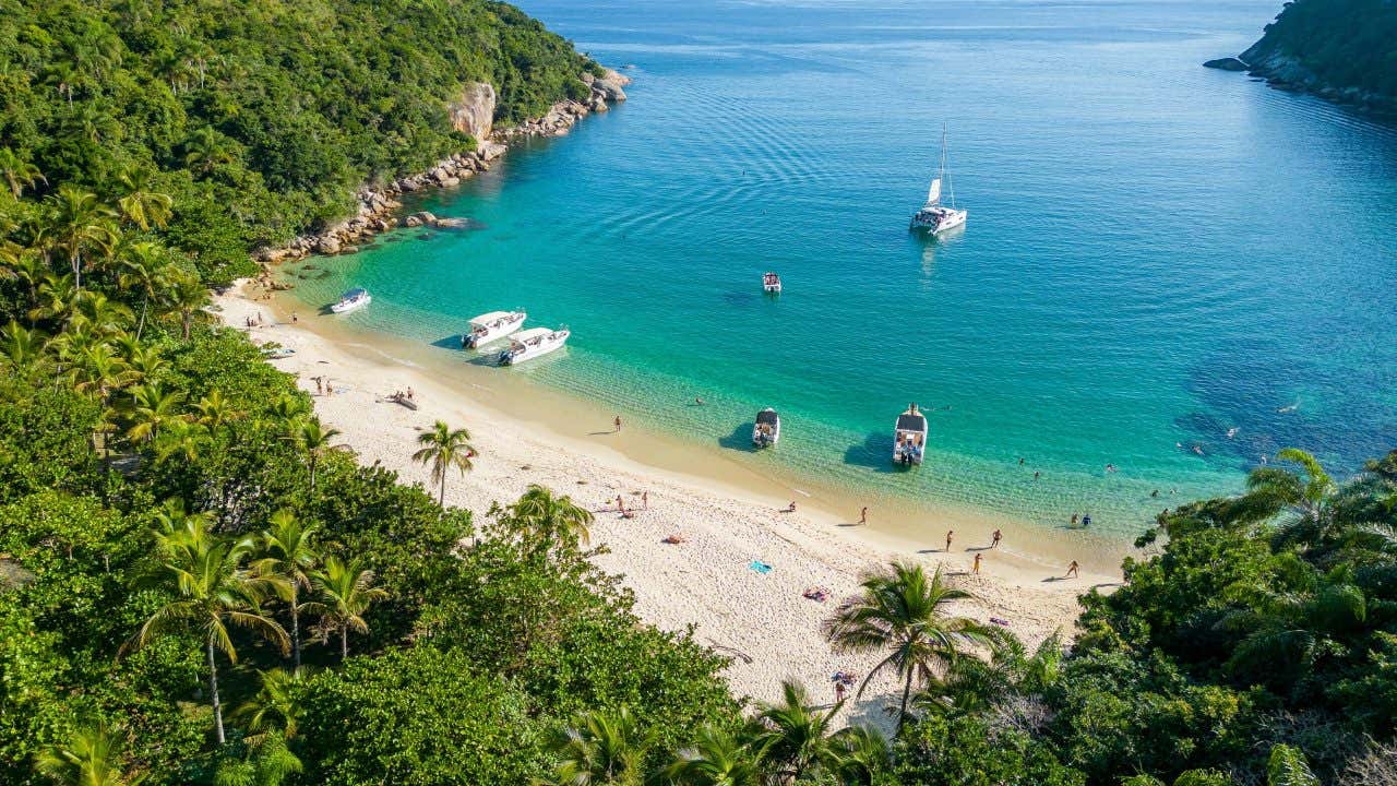 Vista aérea de uma praia com água turquesa e areia branca cercada de vegetação