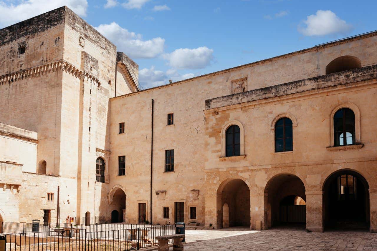 Cortile interno di un maniero medievale circondato da austeri palazzi dalle facciate spoglie, ricoperte di pietra massiccia e levigata
