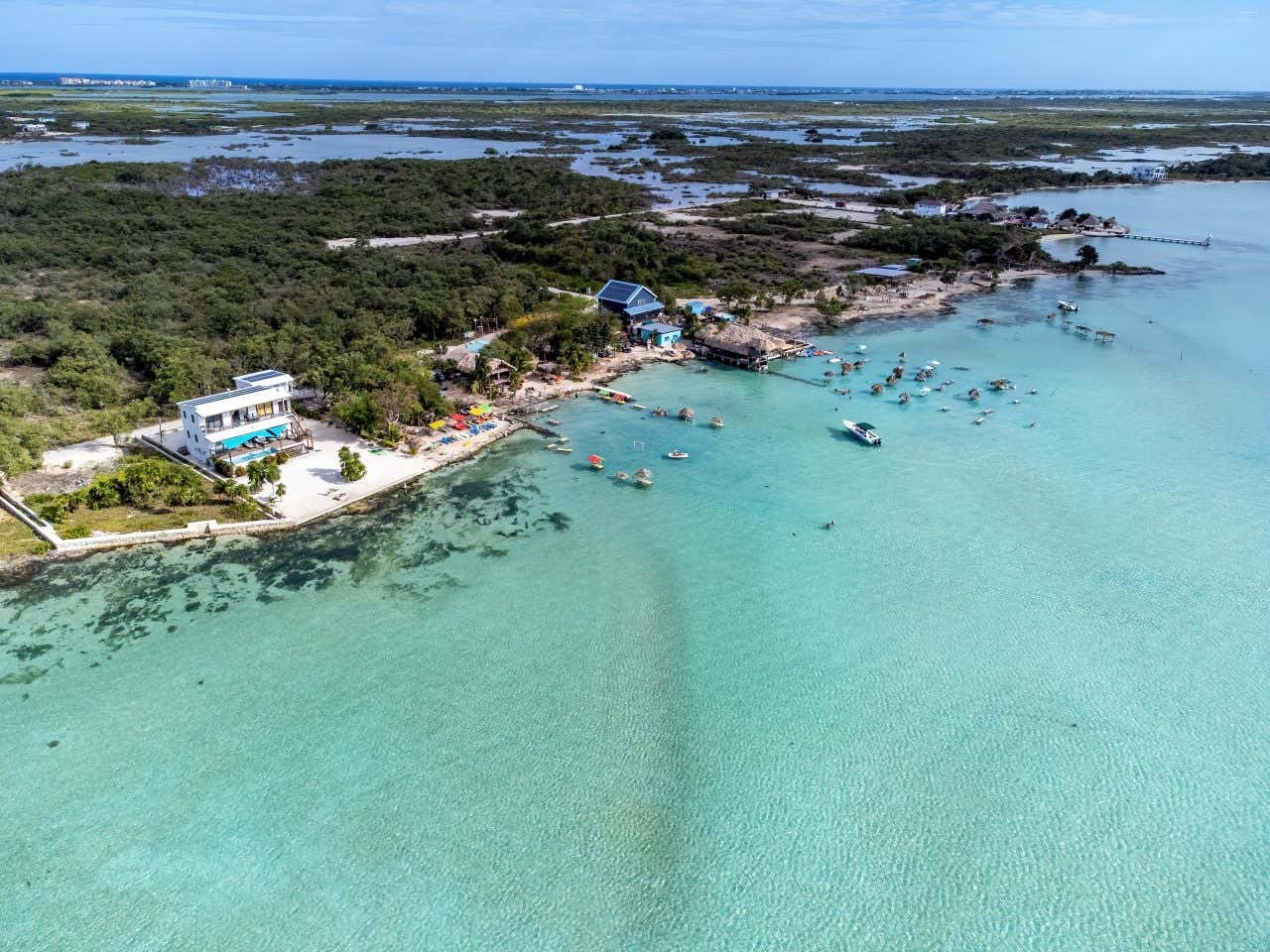 An aerial view of 'Secret Beach' in Belize, with 2 buildings, a dock, a boat, and various umbrellas in view.