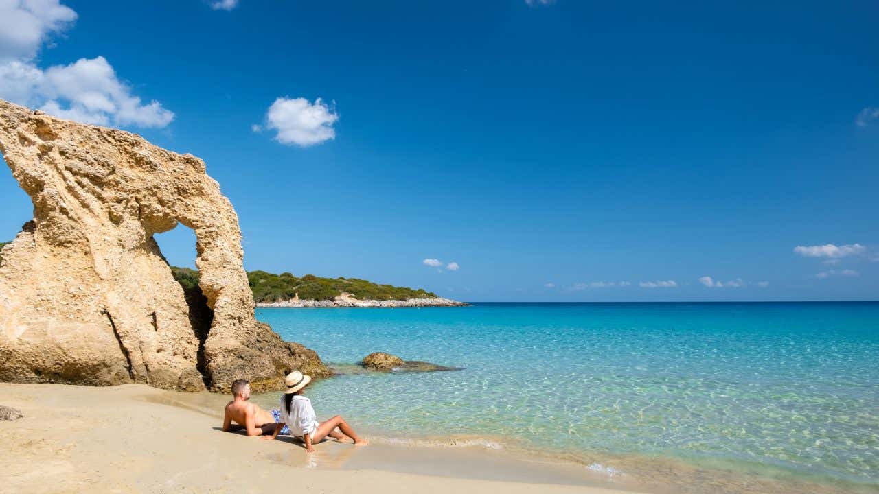Una coppia di bagnanti è sdraiata sul bagnasciuga di una spiaggia cretese dalle acqua trasparenti senza altri turisti nei dintorni