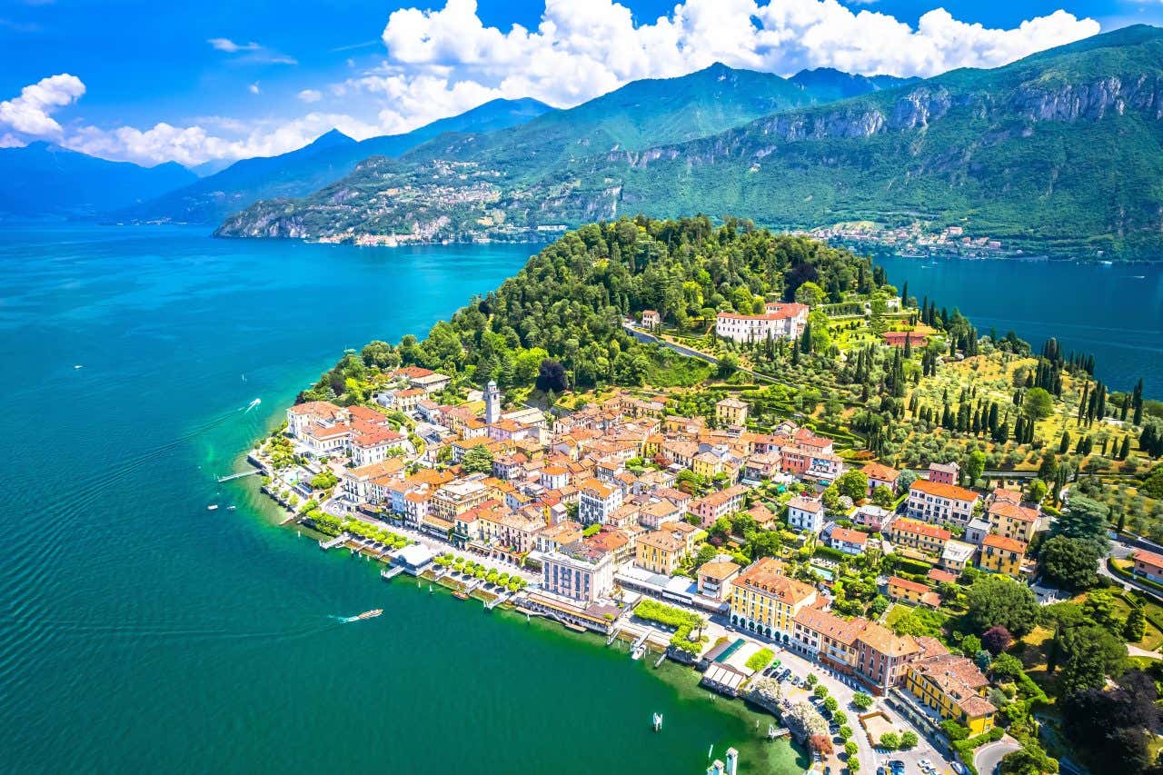 Veduta aerea soleggiata di Bellagio, pittoresca cittadina situata sulla punta del promontorio che divide i due rami del Lago di Como, circondata da acque azzurre e montagne verdi