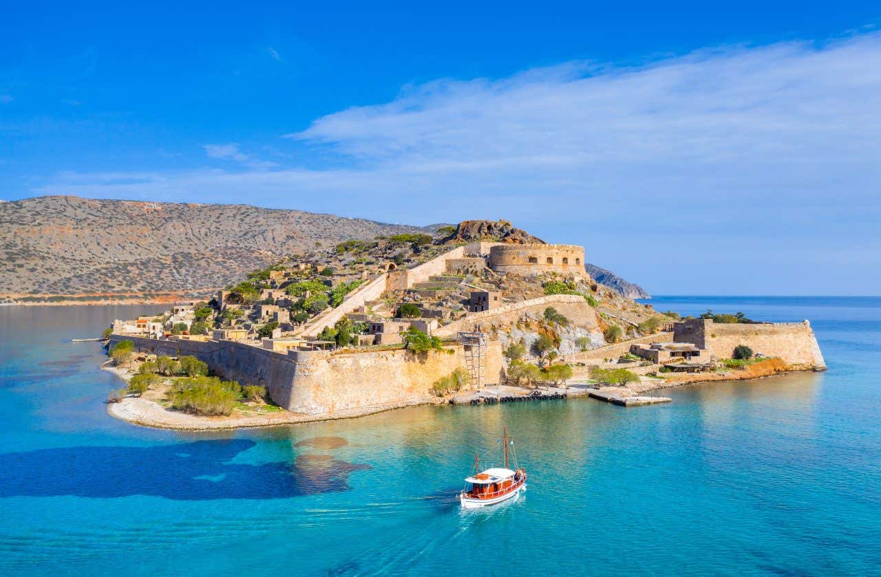 Vue sur l'îlot de Spinalonga avec un bateau naviguant sur les eux turquoise, une activité à faire absolument en Crète