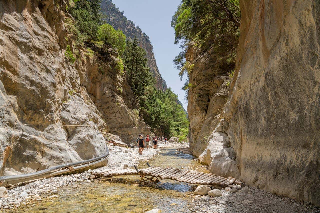 Alcuni escursionisti camminano nei pressi di un torrente, al centro di una gola rocciosa sormontata da boschi in una giornata di sole