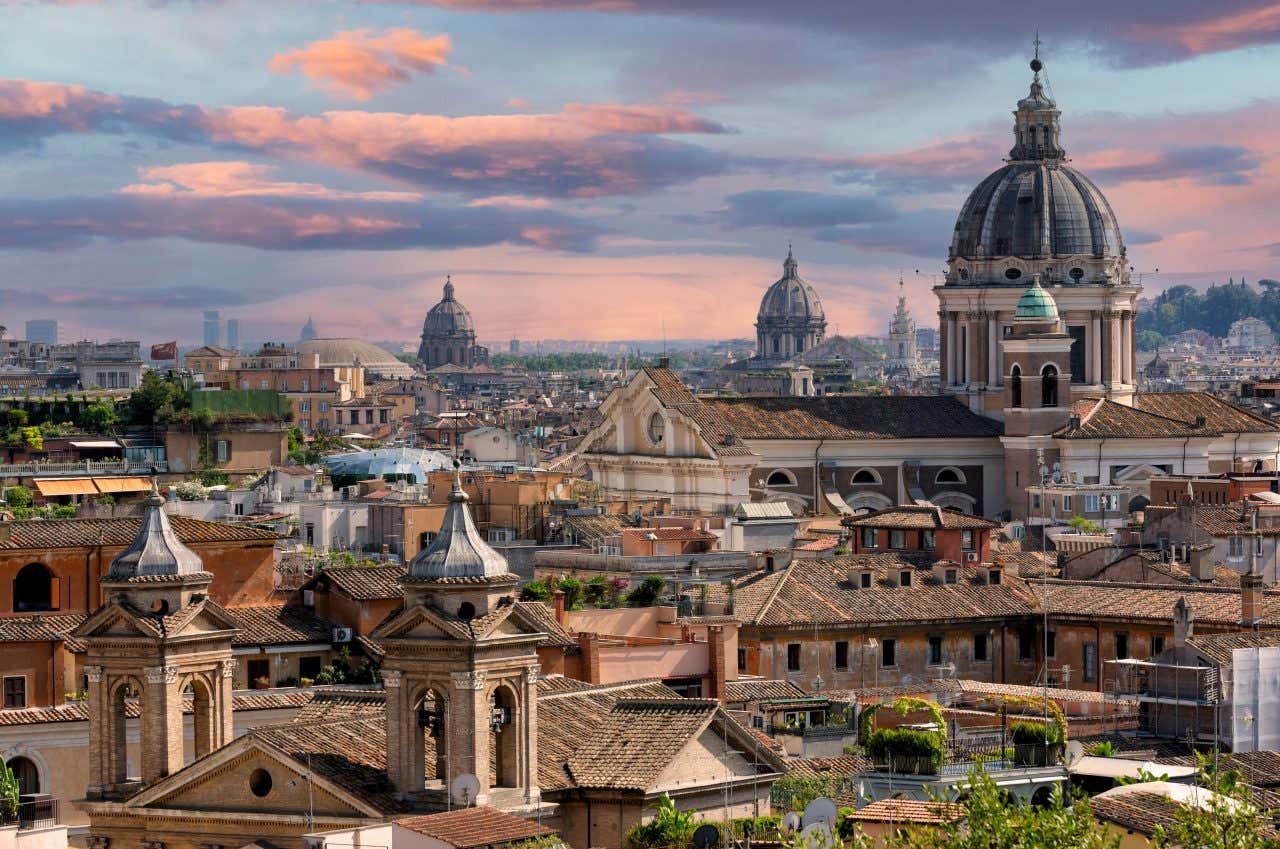 An evening skyline in Rome, Italy, with a pink/blue cloudy sky in the background.