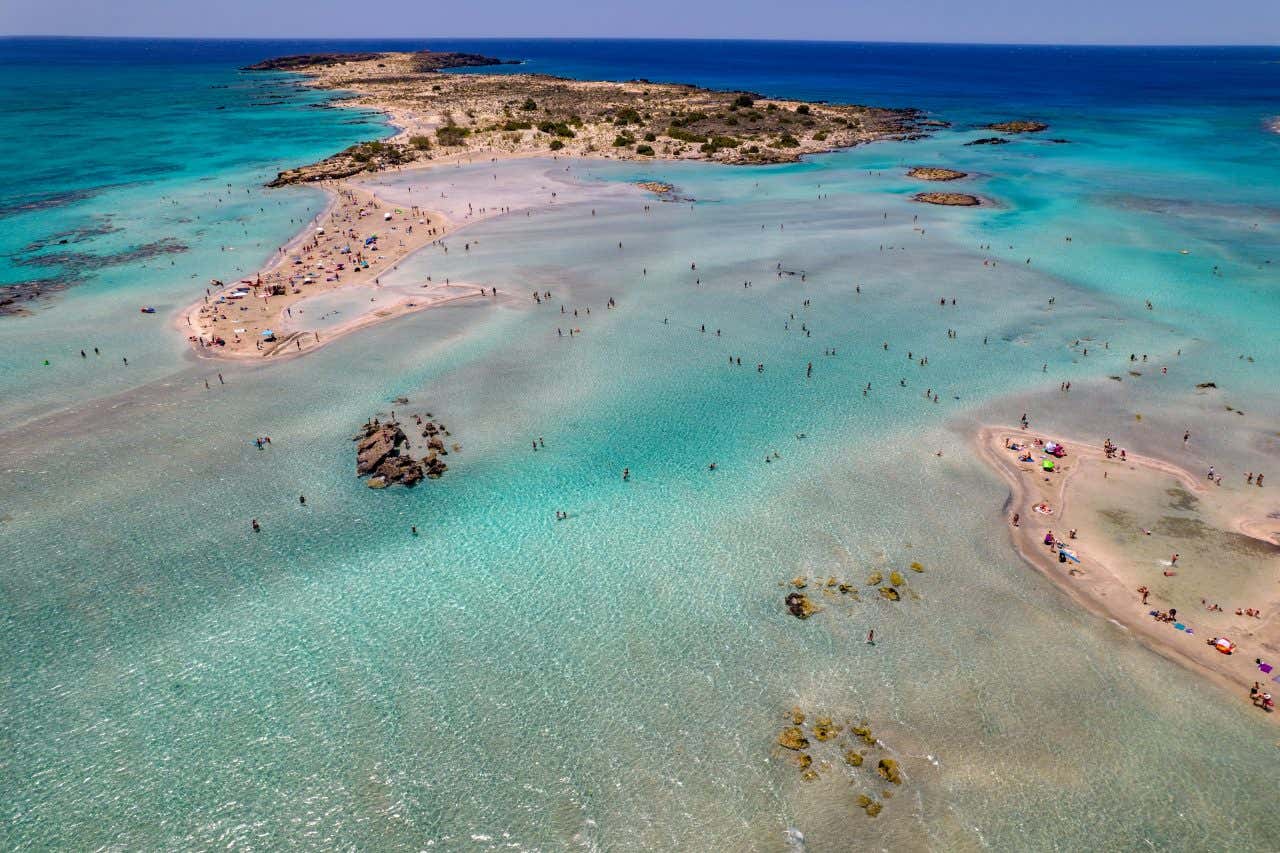 Veduta aerea della spiaggia di Elafonissi a Creta, Grecia, con sabbia chiara, acque turchesi poco profonde e numerosi bagnanti sparsi lungo la riva e nelle lagune