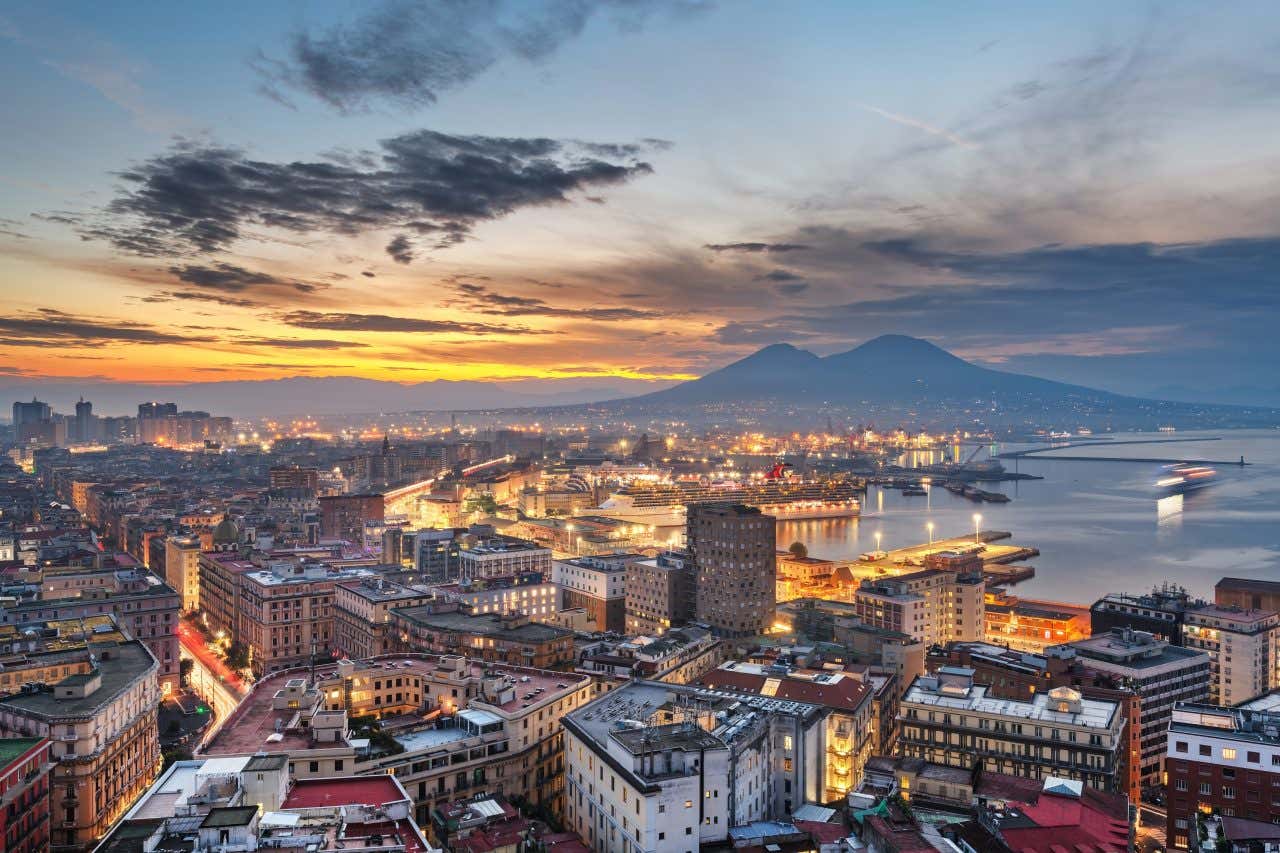 The Naples skyline seen from above as the sun sets over the horizon.