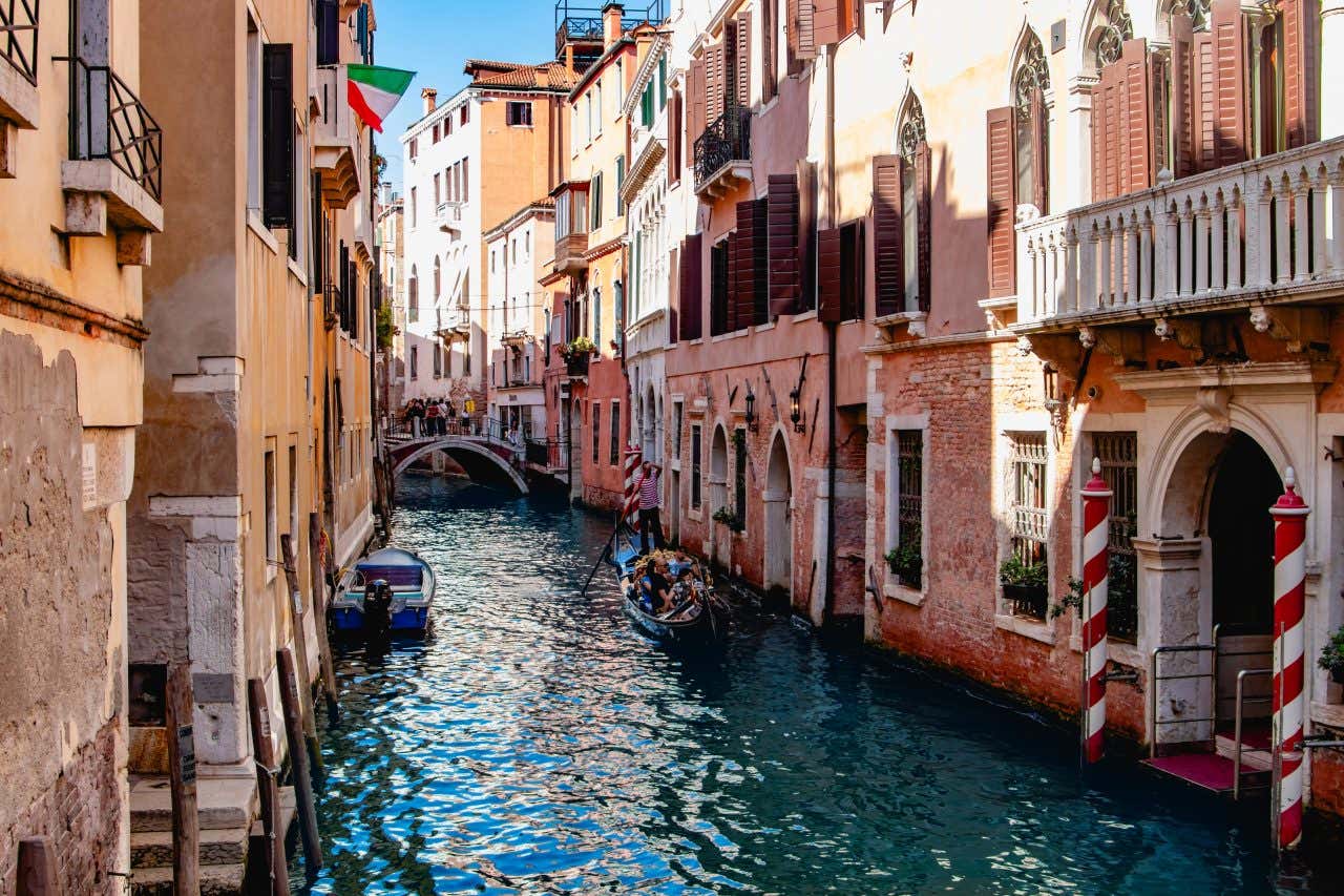 A canal in Venice during the day with the sun shining down into the street.