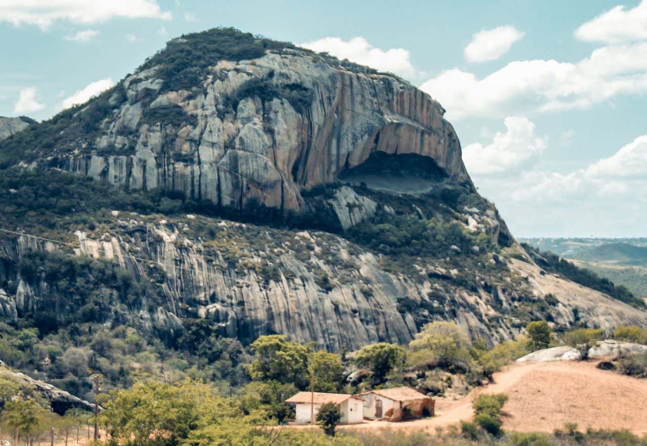 Uma formação rochosa com formato de boca rodeada de uma paisagem semi-árida