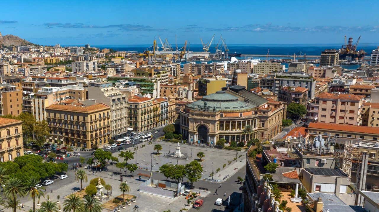 Vista dall'alto di Piazza Politeama, con il teatro Garibaldi e i palazzi che lo circondano, il mare con il porto di Palermo sullo sfondo in un giorno di sole 
