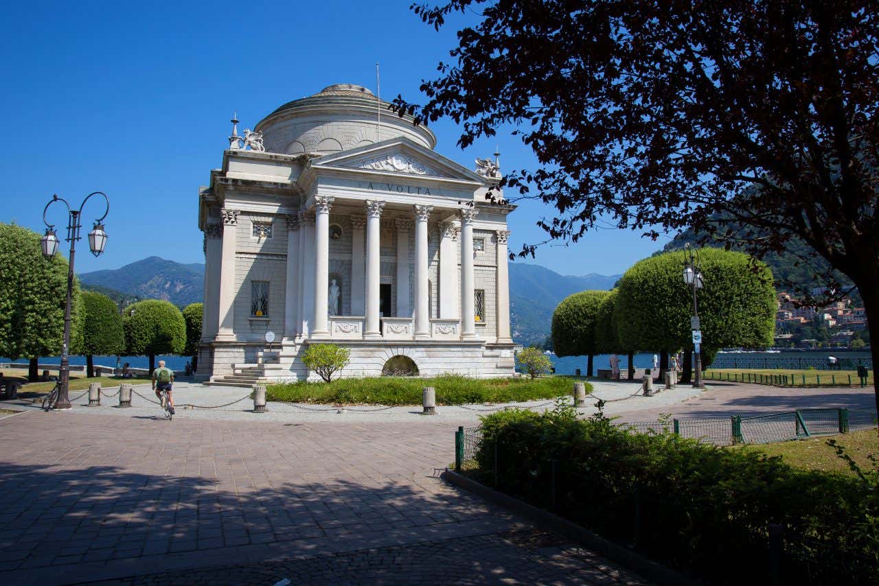 Facciata del Tempio Voltiano a Como, edificio neoclassico ispirato al Pantheon, con pronao sorretto da quattro colonne corinzie e cupola centrale; sullo sfondo, il lago di Como in una luminosa giornata di sole