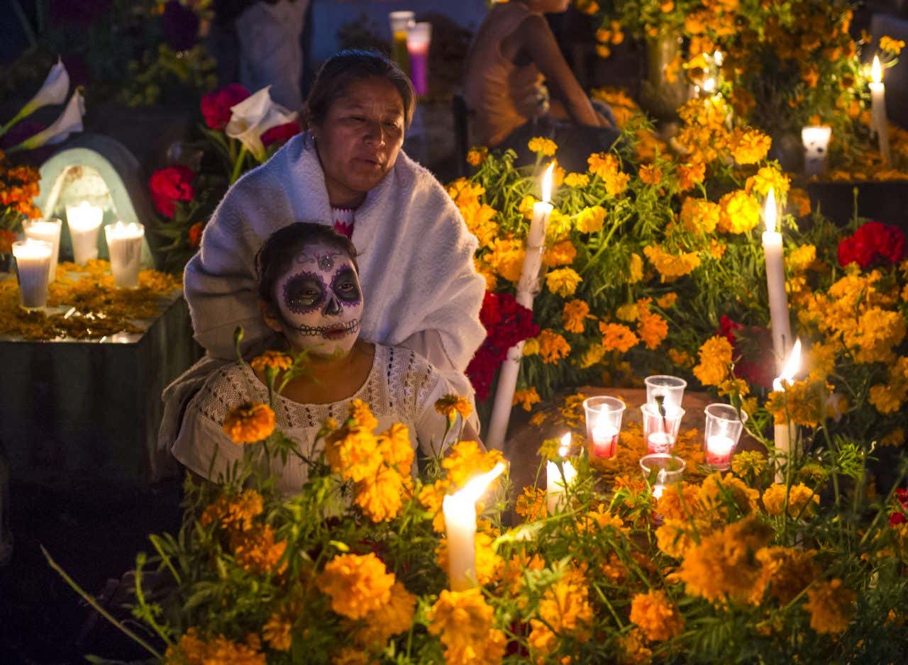 An elaborate altar in Oaxaca, a girl with traditional face pain and her mother looking toward the camera.