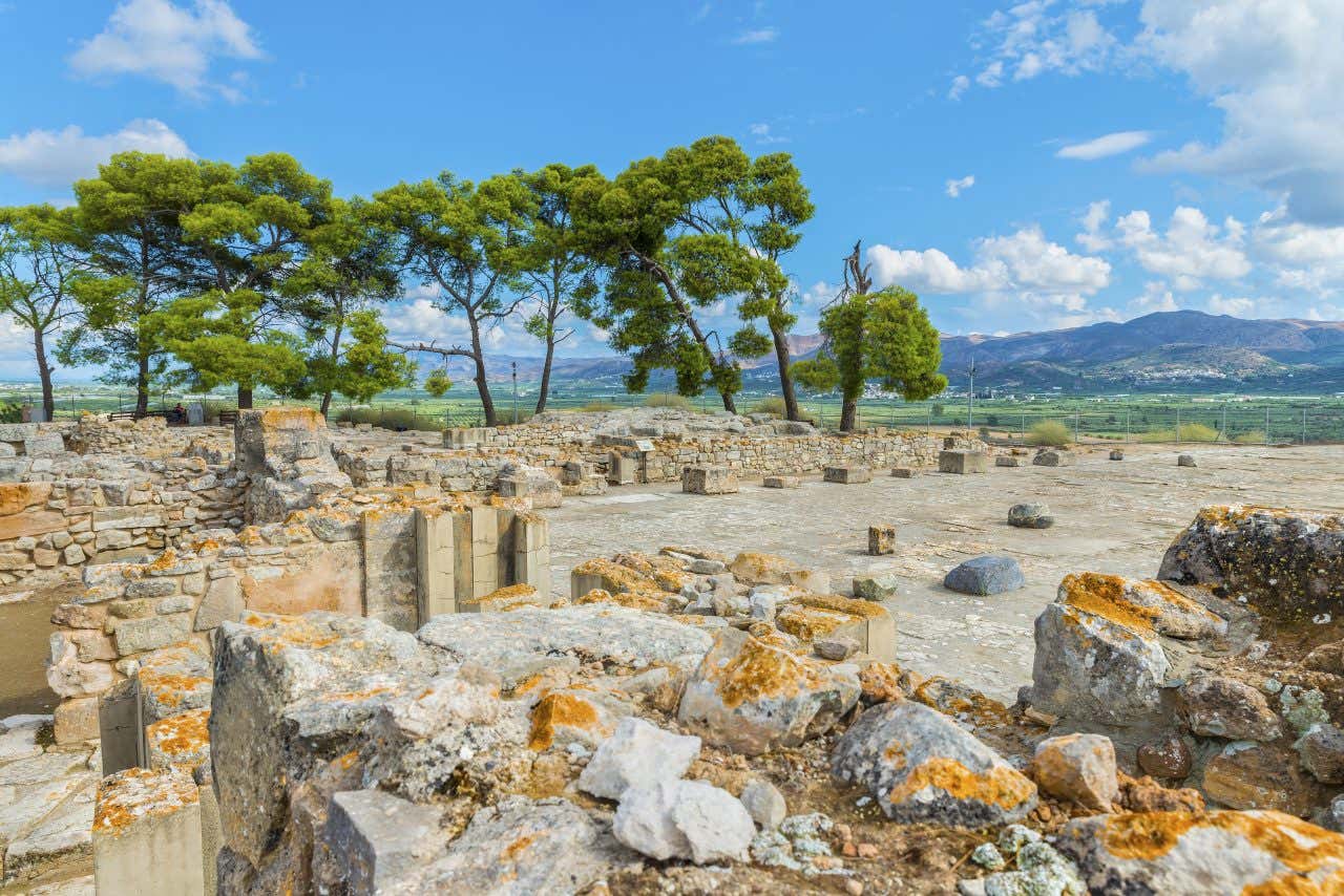Alcuni resti archeologici di quello che era il Palazzo di festo, al centro di una verde vallata circondata da alberi in un giorno di sole