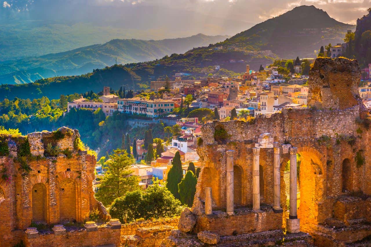 Les ruines du théâtre romain de Taormine en premier plan avec vue sur le village en fin d'après-midi lorsque le soleil descend, une visite à faire absolument en Sicile