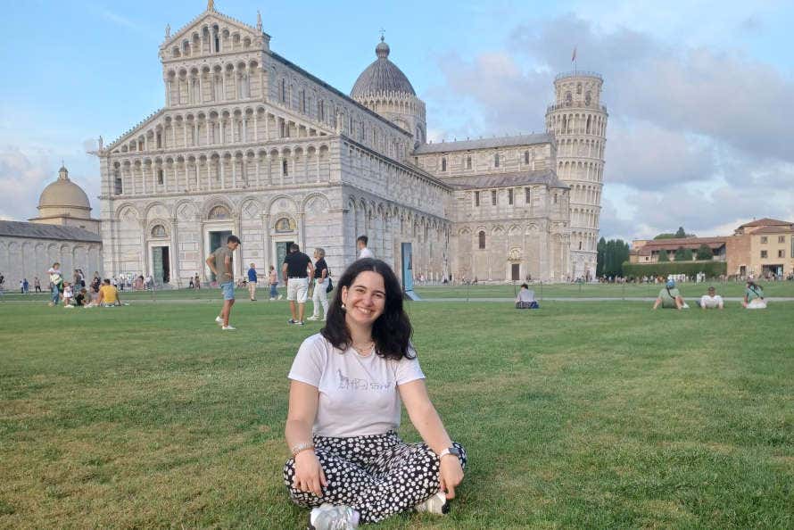 Una chica sentada en el césped de la plaza de los Milagros de Pisa, ante la Torre Inclinada y el Duomo