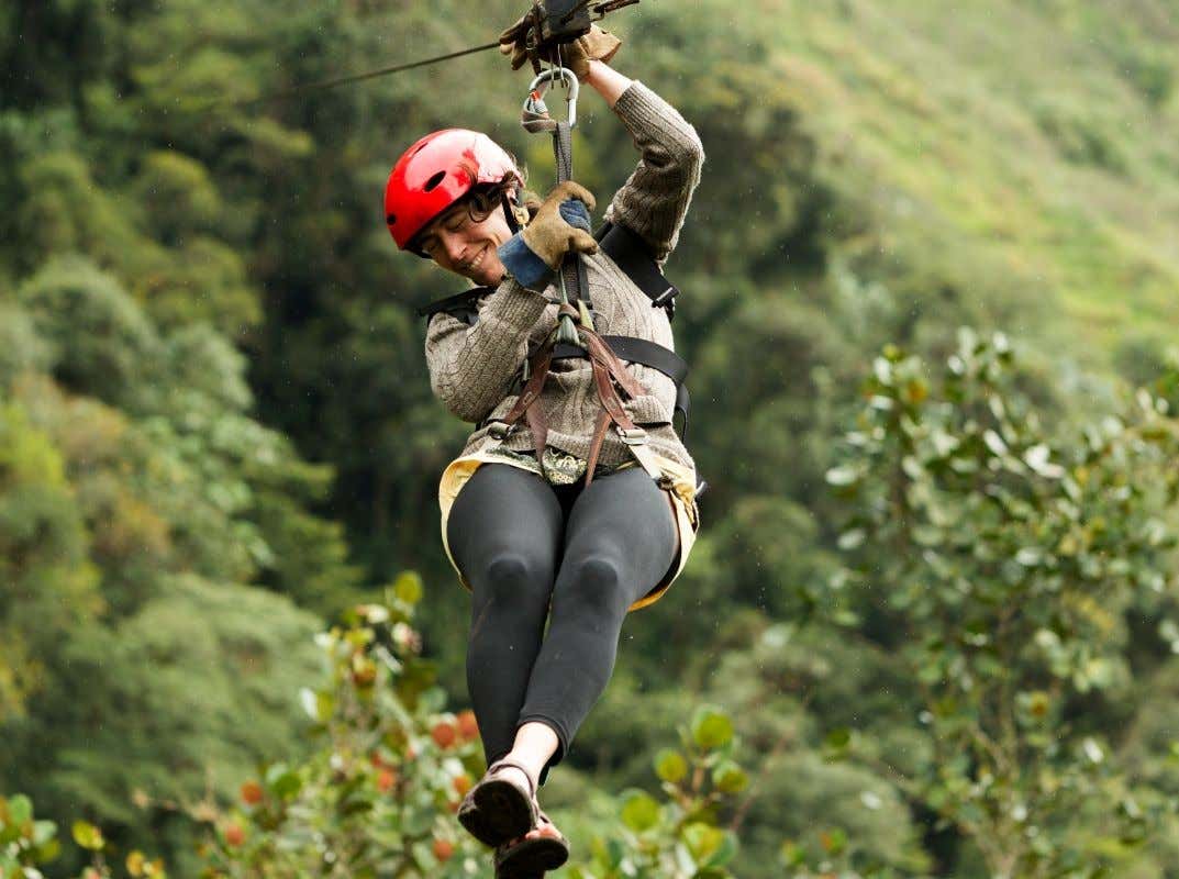 Una mujer ríe mientras se lanza en tirolina en medio de un bosque