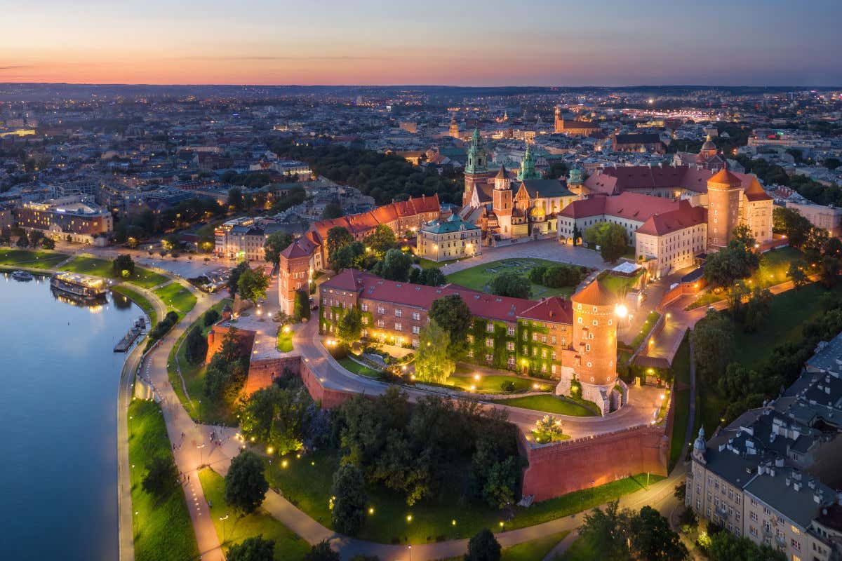 Vista aérea y nocturna del castillo de Cracovia iluminado y junto a un río