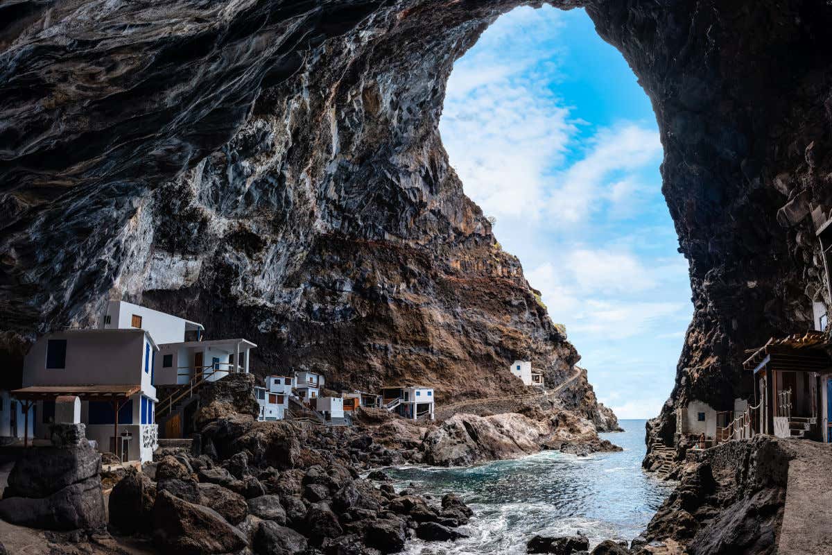 Interior de una gran cueva marina con varias casas blancas de pescadores que son iluminadas por la luz que entra a través de la gruta