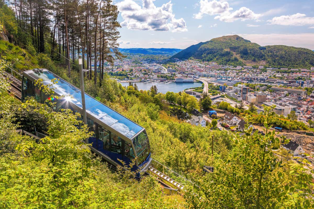 El funicular del monte Fløyen descendiendo por una ladera con vistas a otras colinas, parte del fiordo y a las casas de Bergen