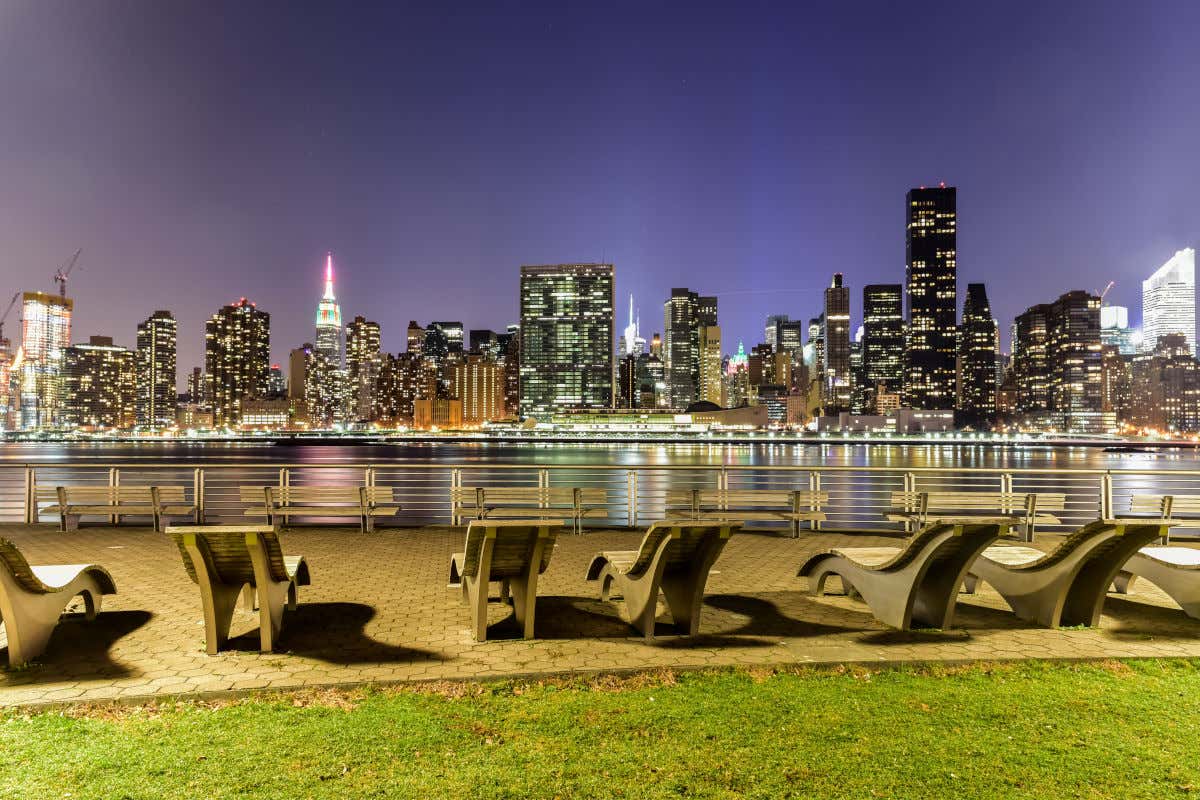 Varios bancos individuales en una plaza sin gente con vistas a los rascacielos de Nueva York por la noche