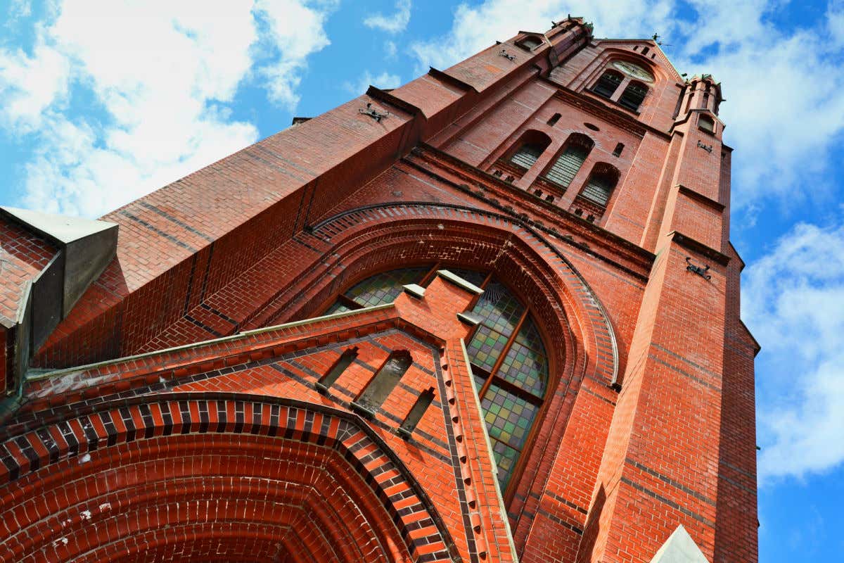 Torre de una iglesia de ladrillo rojizo con vidrieras en un día despejado con pocas nubes