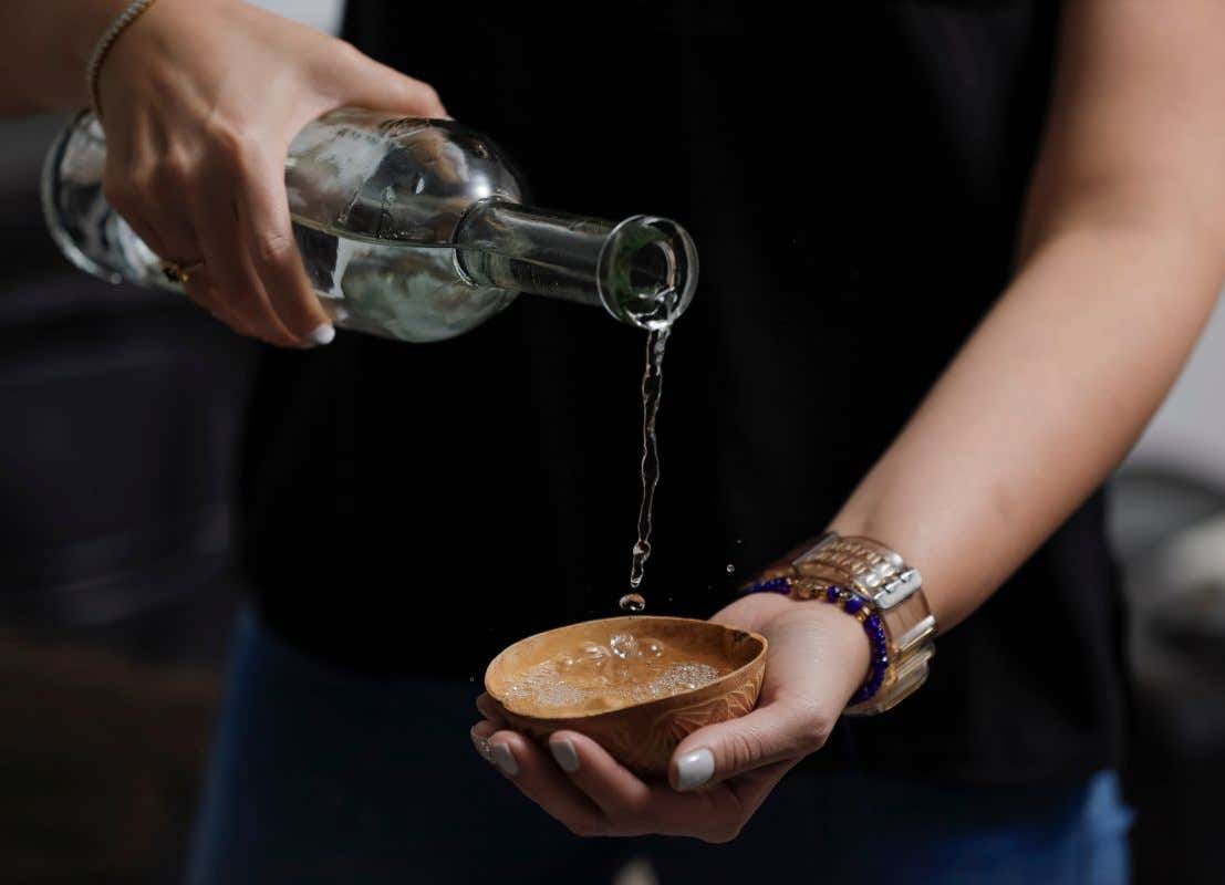 Unas manos femeninas sirven un aguardiente en un vaso de madera