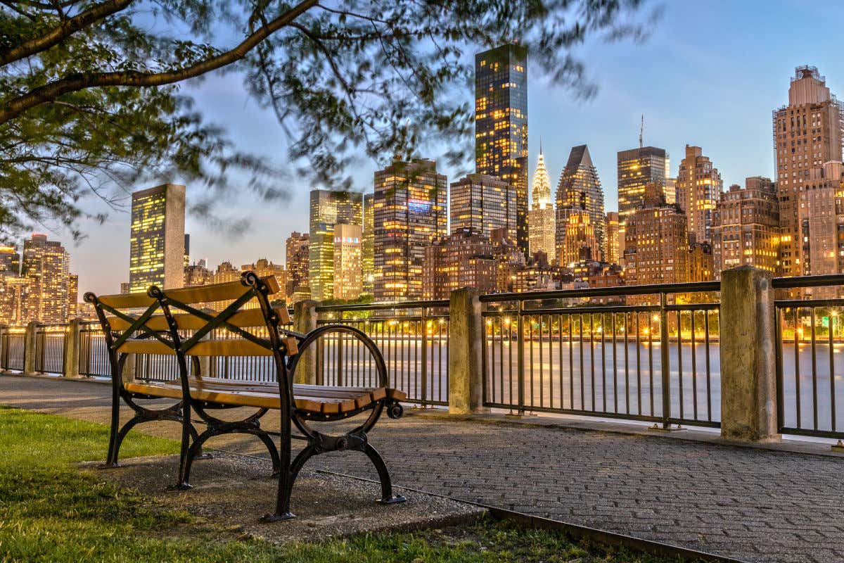 Un banco en un paseo marítimo con vistas a los rascacielos de Nueva York iluminados