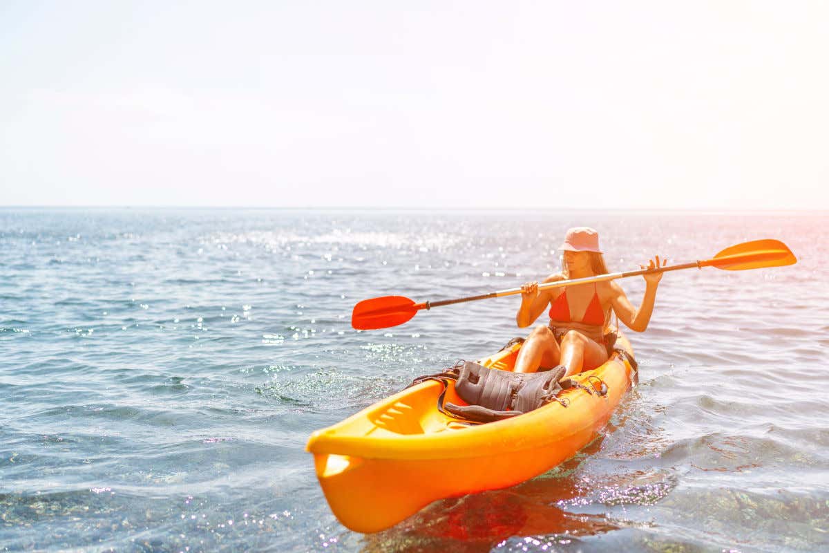 Una mujer en bikini y con gorro remando en un kayak de color naranja