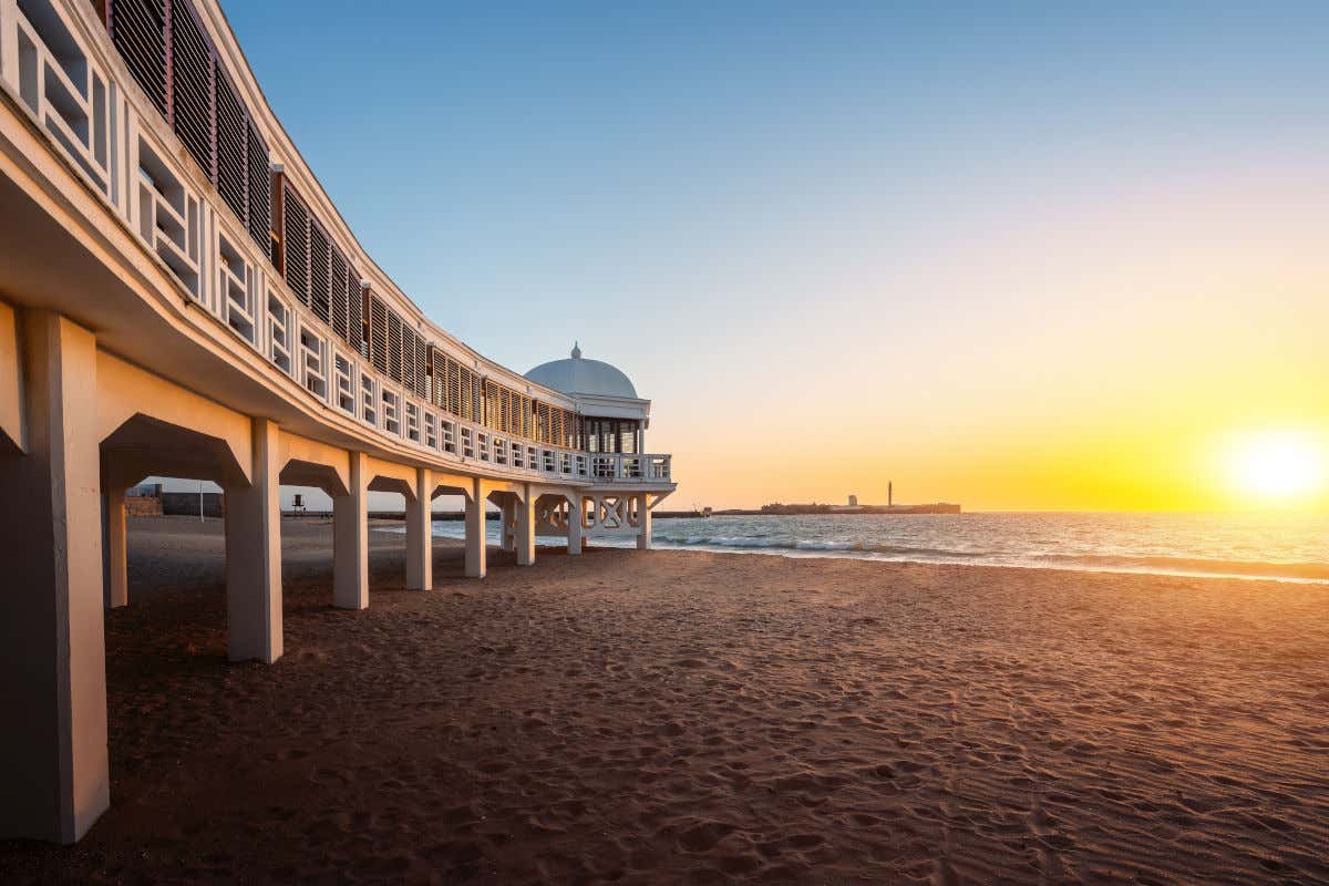 Atardecer en la playa de La Caleta, una bahía de arena con vistas a un faro y un castillo de Cádiz