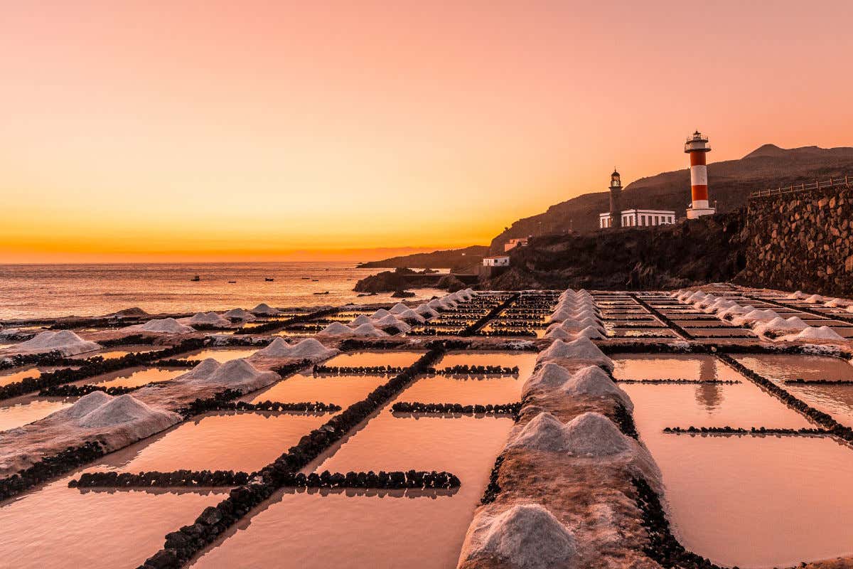 Las salinas de Fuencaliente con varias montañas de sal al atardecer y junto a un faro