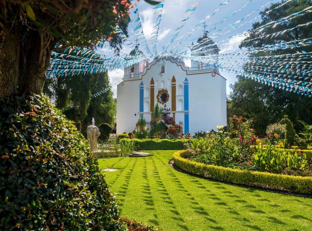 Un parque verde con flores y árboles frente a una iglesia católica