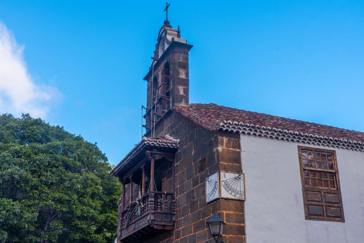 Una iglesia de pequeño tamaño, con fachada de piedra, ventana y balcón de madera, así como un campanario de reducidas dimensiones