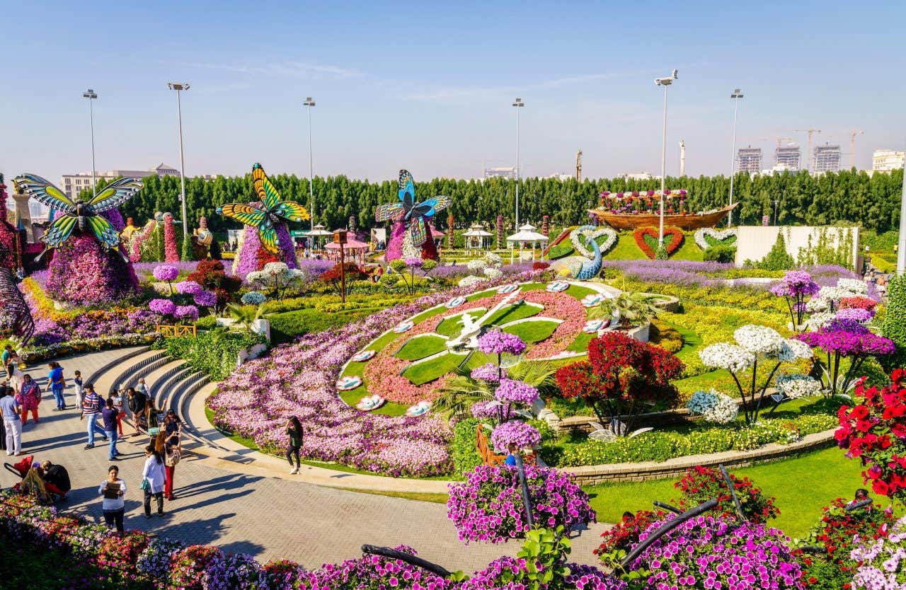 Jardim florido com muitas cores, e um relógio de flores ao meio. Borboletas gigantes enfeitando os arbustos
