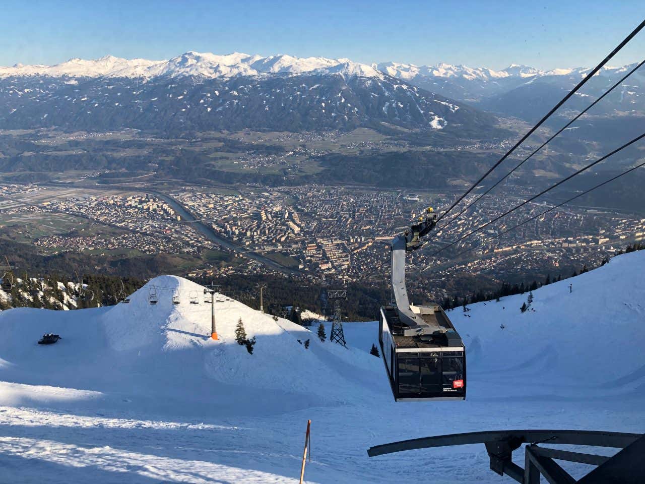 La cabina di una funicolare risale il fianco innevato della montagna mentre a valle di vede Innsbruck con il fiume Inn che attraversa la città