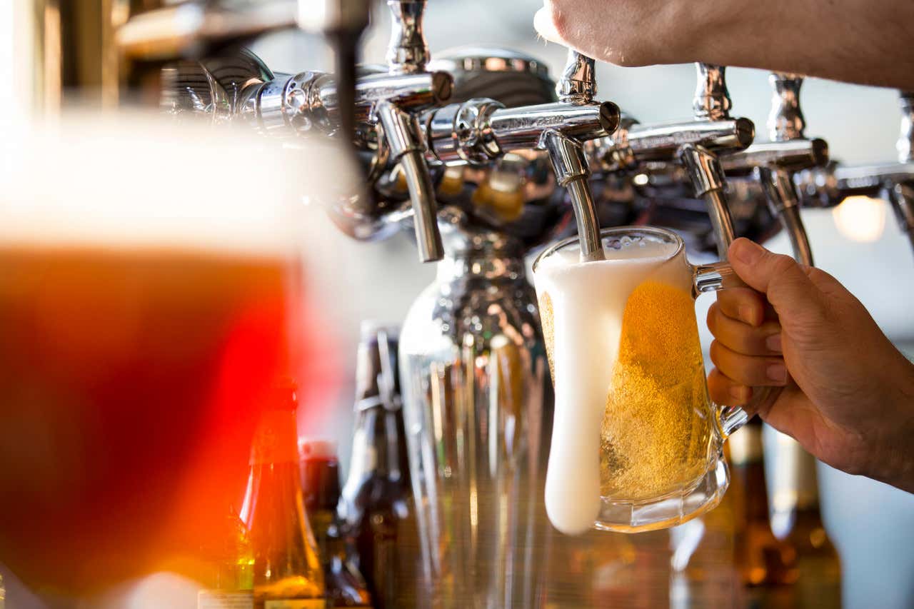 As mãos de uma pessoa servindo cerveja em um copo