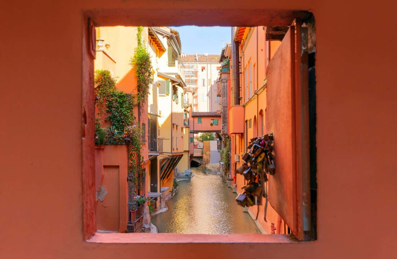 Canal au milieu d'une rue aux bâtiments rose orangé à Bologne, une ville où aller en Italie