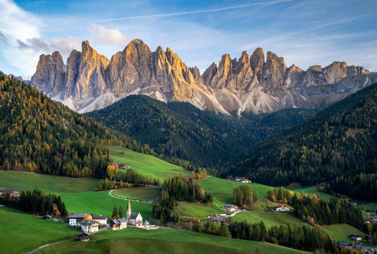 Vue sur les Dolomites, incontournables en Italie, avec quelques habitations entourées de champs et de forêts