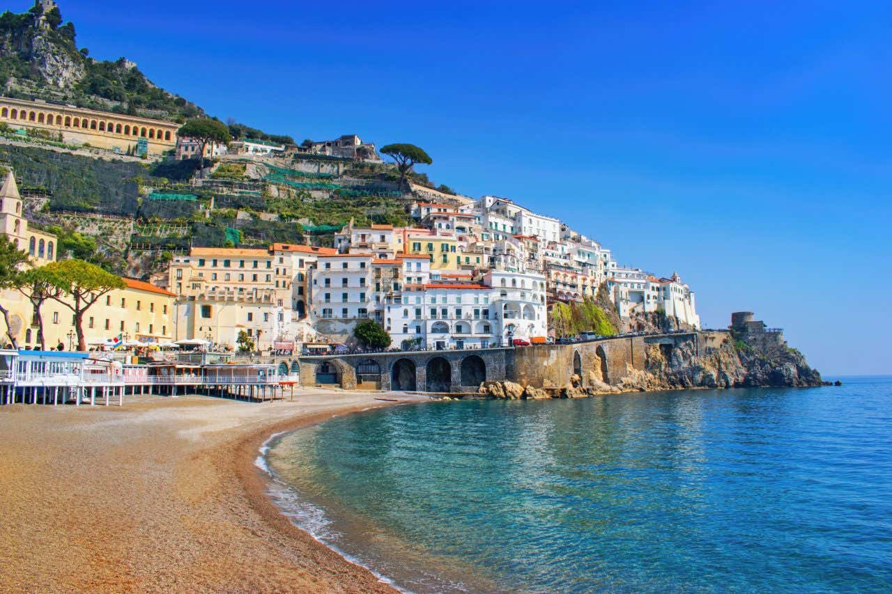 A shot of a town in the Amalfi Coast taken from an empty beach, with a clear blue sky in the background.