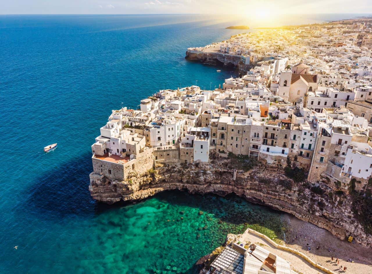 An aerial view of Polignano a Mare with turquoise waters and a boat near the base of the cliff.