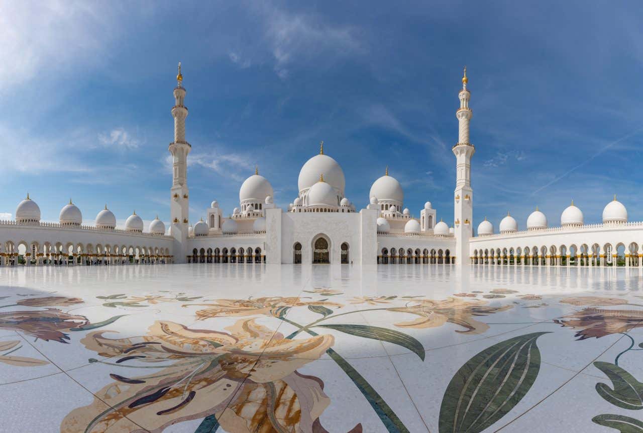 A Grande Mesquita de Abu Dhabi, uma das maiores e mais bonitas do mundo, com chão de mármore branco decorado, dois miranetes e diversas cúpulas brancas