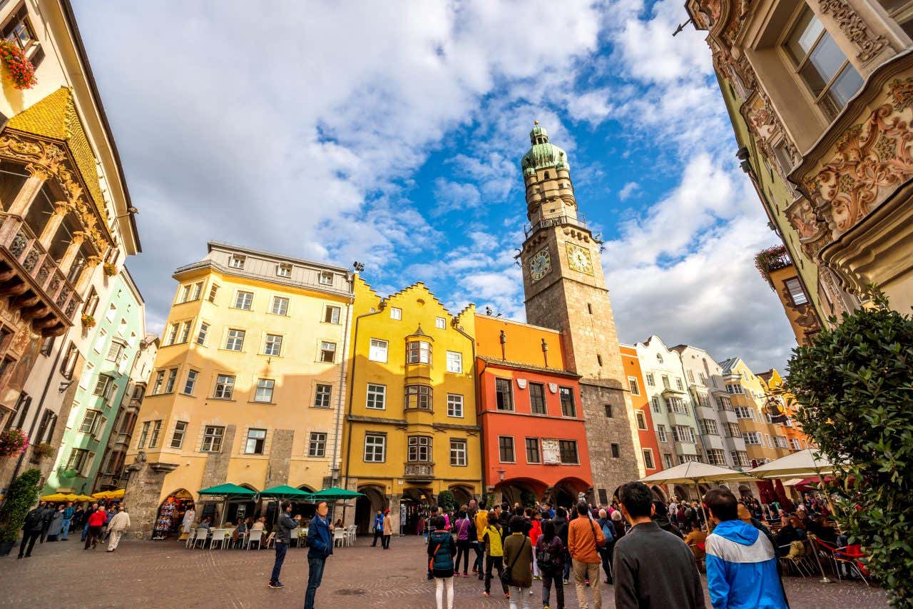Una piazza del centro storico di Innsbruck con diversi turisti a passeggio, palazzi medievali colorati e una torre con orologio